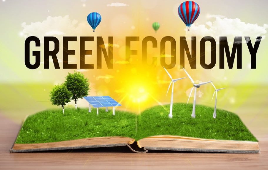 An image alluding to the green economy, with an open book, with grass forming pages. On the left side page are two trees and a solar panel. On the right side, three wind turbines. In the center is the sun, above it is written in black Green Economy and above the letters are three hot air balloons.
