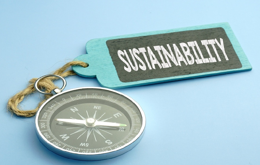 Image of a compass and a blue wooden keyring with the word sustainability in white letters on a black background.